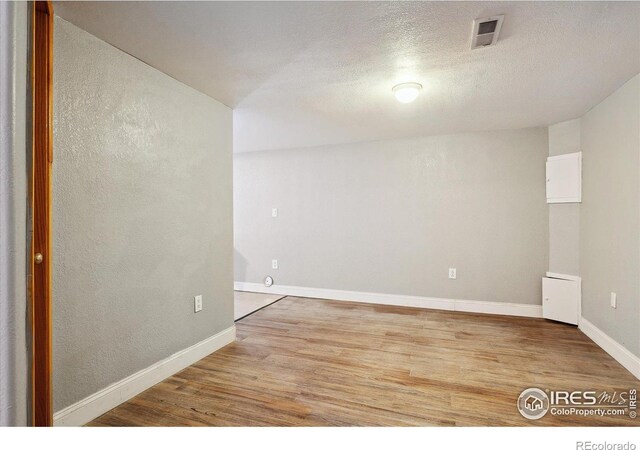 unfurnished room with baseboards, a textured ceiling, visible vents, and wood finished floors