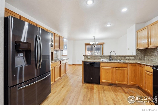 kitchen with black dishwasher, light wood-style flooring, a sink, stainless steel fridge, and a peninsula