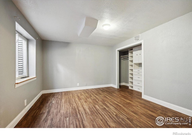 unfurnished bedroom with baseboards, visible vents, wood finished floors, a textured ceiling, and a closet