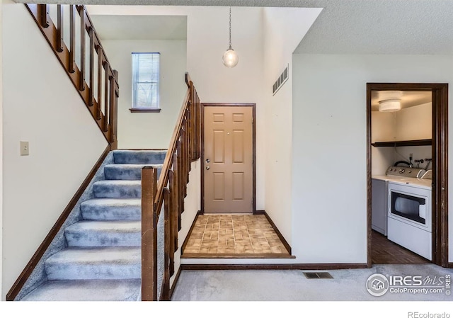 carpeted foyer entrance with a textured ceiling and washing machine and clothes dryer