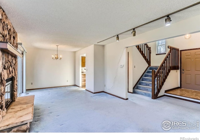 unfurnished living room featuring a fireplace, a chandelier, carpet, and a textured ceiling