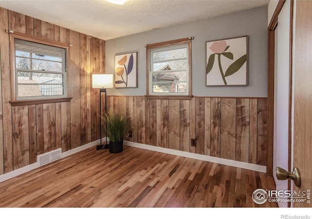 empty room with wooden walls, hardwood / wood-style floors, and a textured ceiling