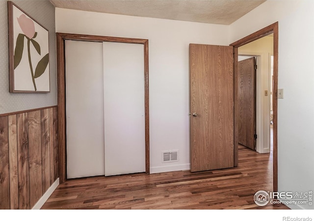 unfurnished bedroom with dark hardwood / wood-style floors, wood walls, a textured ceiling, and a closet