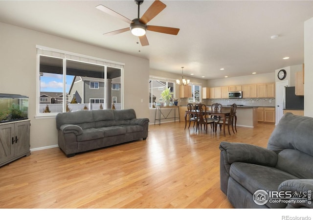 living room featuring ceiling fan with notable chandelier and light hardwood / wood-style flooring