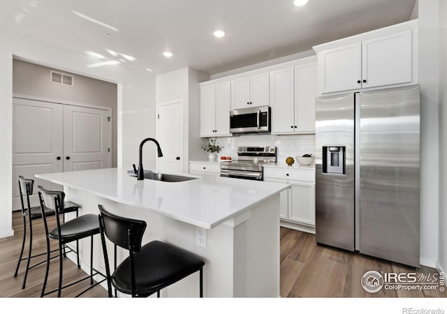 kitchen with sink, white cabinets, a kitchen breakfast bar, stainless steel appliances, and a center island with sink