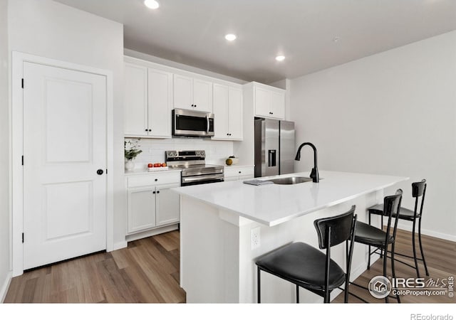 kitchen featuring white cabinetry, stainless steel appliances, a breakfast bar, and a center island with sink