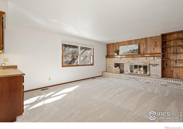 unfurnished living room with a brick fireplace, sink, light colored carpet, and wood walls