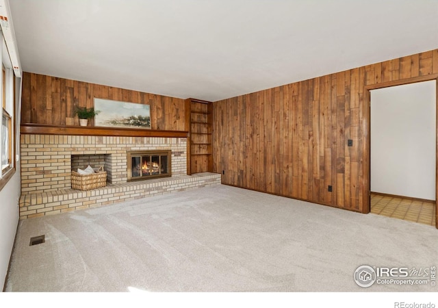 unfurnished living room with light carpet, a brick fireplace, and wood walls