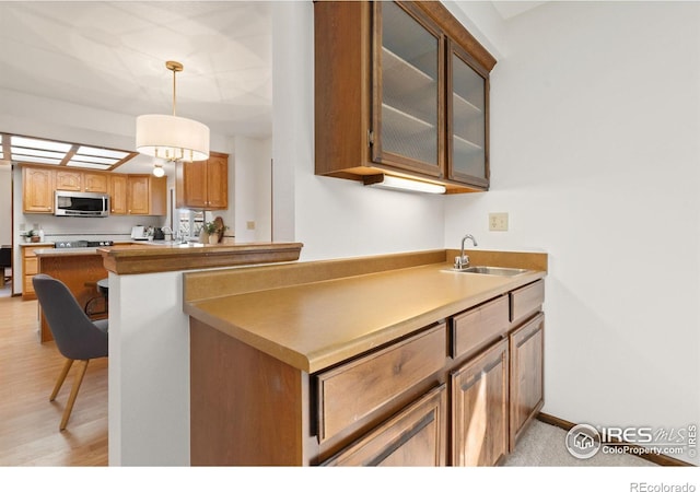 kitchen with sink, a kitchen breakfast bar, decorative light fixtures, kitchen peninsula, and light wood-type flooring