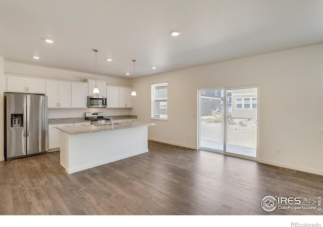 kitchen featuring white cabinetry, hanging light fixtures, appliances with stainless steel finishes, an island with sink, and light stone countertops