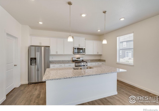 kitchen with white cabinetry, appliances with stainless steel finishes, light stone countertops, and a kitchen island with sink