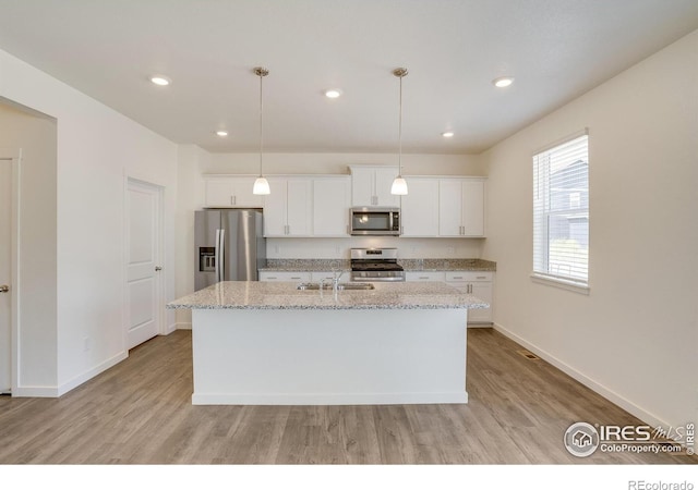 kitchen featuring white cabinetry, light stone counters, a kitchen island with sink, and stainless steel appliances