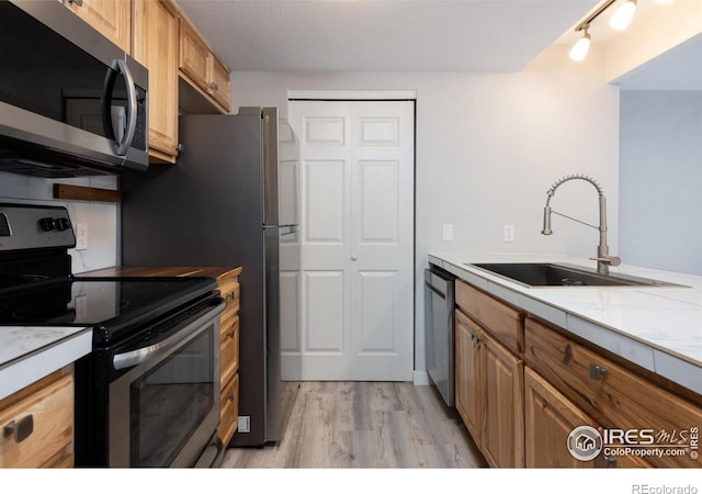 kitchen with appliances with stainless steel finishes, sink, and light hardwood / wood-style flooring