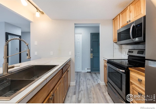 kitchen with sink, light hardwood / wood-style floors, baseboard heating, and appliances with stainless steel finishes