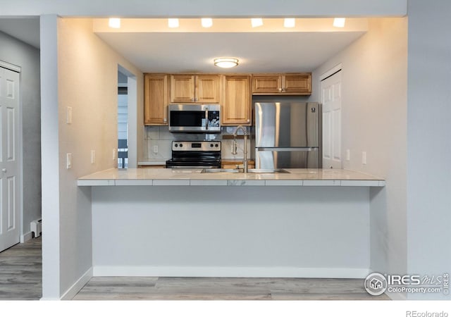 kitchen featuring sink, backsplash, kitchen peninsula, stainless steel appliances, and light hardwood / wood-style flooring