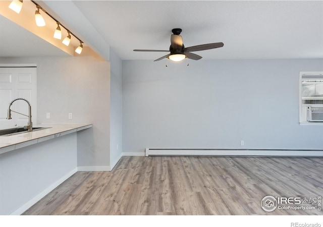 interior space with light wood-type flooring, ceiling fan, sink, and a baseboard heating unit