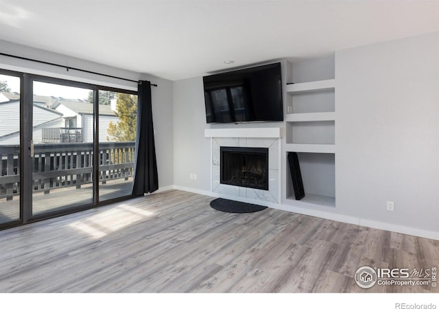 unfurnished living room featuring built in shelves, light hardwood / wood-style flooring, and a tile fireplace