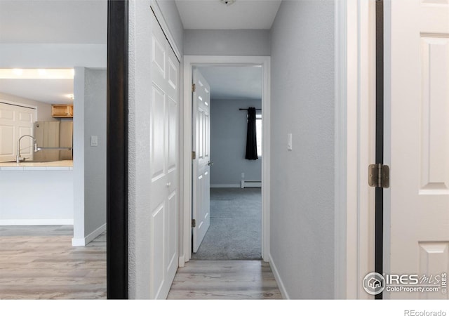 corridor featuring sink, a baseboard radiator, and light hardwood / wood-style floors