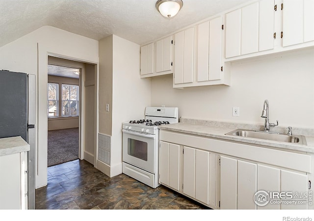 kitchen featuring sink, white gas range oven, stainless steel refrigerator, white cabinetry, and a textured ceiling