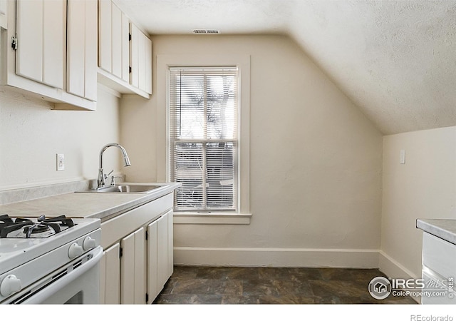 kitchen with sink, a textured ceiling, white cabinets, vaulted ceiling, and white gas stove