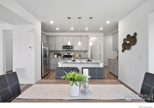 kitchen with pendant lighting, a center island with sink, gray cabinetry, and appliances with stainless steel finishes