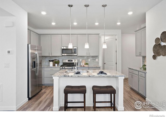 kitchen featuring gray cabinets, decorative backsplash, hanging light fixtures, stainless steel appliances, and light stone countertops