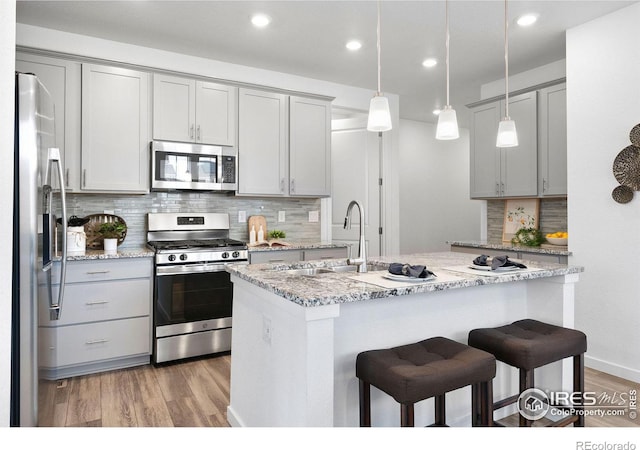 kitchen featuring light stone counters, hanging light fixtures, gray cabinets, stainless steel appliances, and light hardwood / wood-style floors