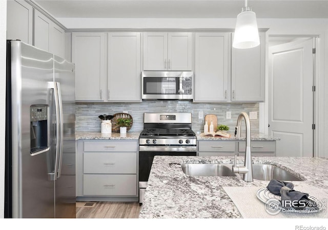 kitchen with pendant lighting, sink, backsplash, stainless steel appliances, and light stone countertops