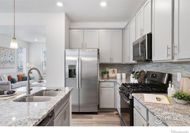 kitchen with sink, light hardwood / wood-style flooring, appliances with stainless steel finishes, hanging light fixtures, and light stone counters