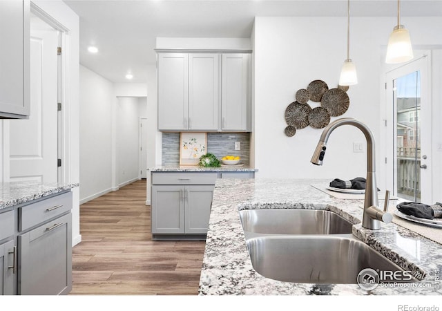 kitchen with sink, gray cabinetry, hanging light fixtures, light hardwood / wood-style floors, and decorative backsplash