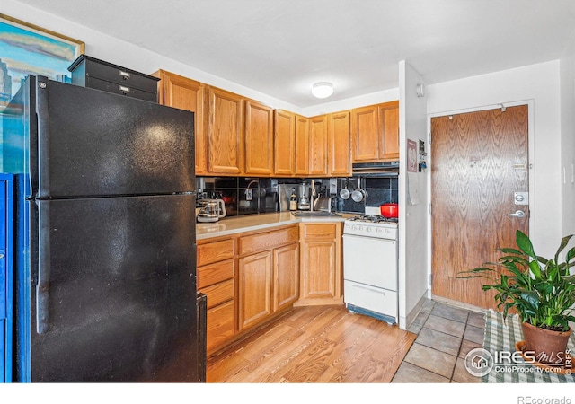 kitchen with black refrigerator, tasteful backsplash, sink, white range with gas cooktop, and light hardwood / wood-style floors