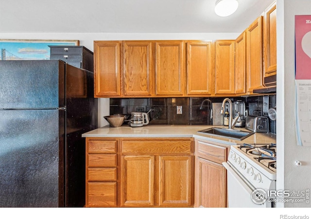 kitchen with tasteful backsplash, black fridge, sink, and white gas range oven