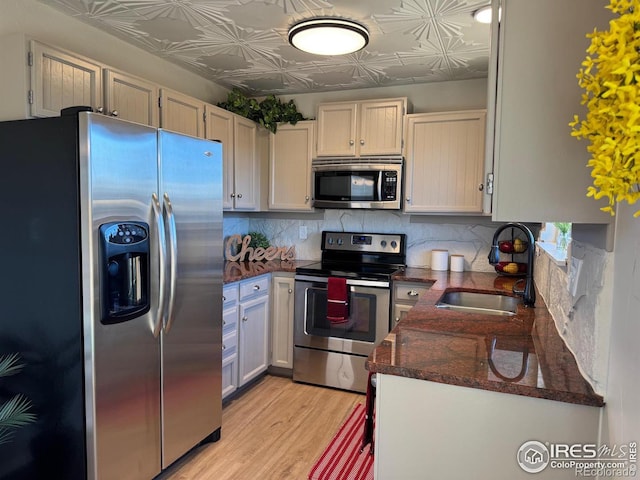 kitchen featuring sink, light hardwood / wood-style flooring, appliances with stainless steel finishes, decorative backsplash, and white cabinets