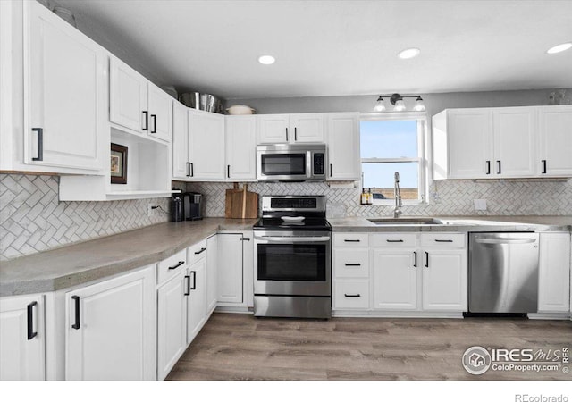 kitchen featuring sink, hardwood / wood-style flooring, appliances with stainless steel finishes, tasteful backsplash, and white cabinets