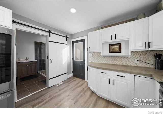 kitchen featuring tasteful backsplash, a barn door, white cabinets, and light wood-type flooring