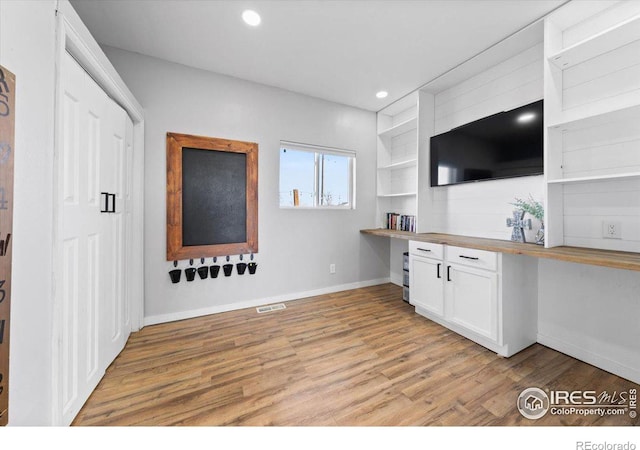 interior space featuring wooden counters, built in desk, light hardwood / wood-style flooring, and white cabinets