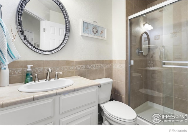 bathroom with a shower with door, vanity, tile walls, and toilet