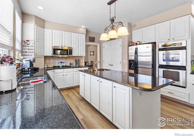 kitchen featuring sink, pendant lighting, stainless steel appliances, a kitchen island with sink, and white cabinets