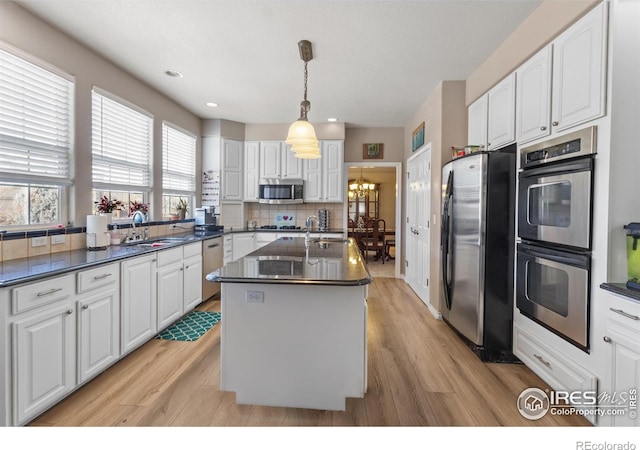 kitchen featuring sink, white cabinetry, stainless steel appliances, a kitchen island with sink, and backsplash