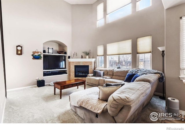 carpeted living room with a tiled fireplace and a high ceiling