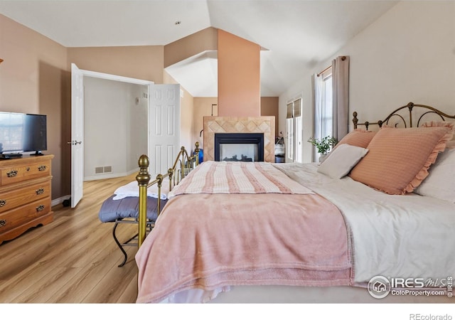 bedroom featuring a tiled fireplace, lofted ceiling, and light hardwood / wood-style flooring