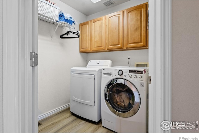 clothes washing area featuring washer and dryer, light hardwood / wood-style floors, and cabinets