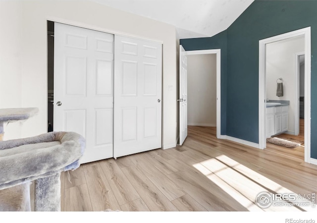 bedroom featuring ensuite bathroom, vaulted ceiling, a closet, and light wood-type flooring