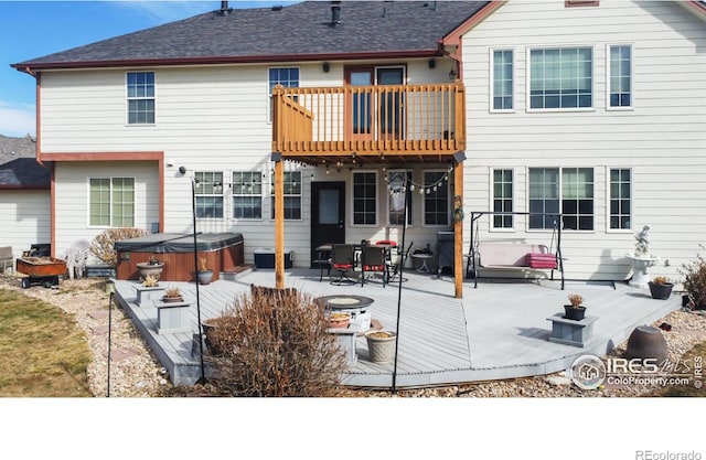 rear view of property featuring a fire pit, a deck, a patio area, a hot tub, and a balcony