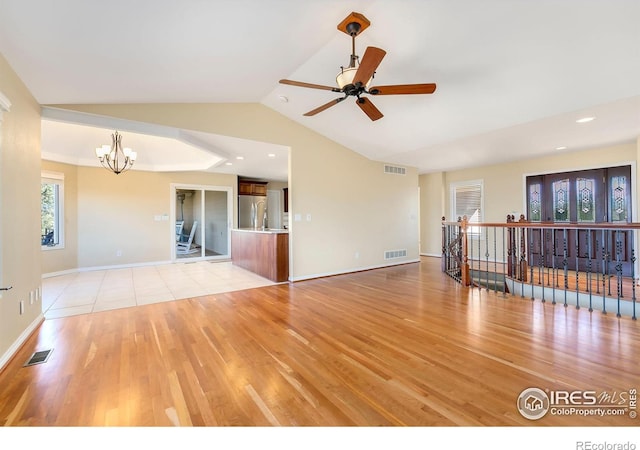 empty room with light hardwood / wood-style flooring, ceiling fan with notable chandelier, and vaulted ceiling