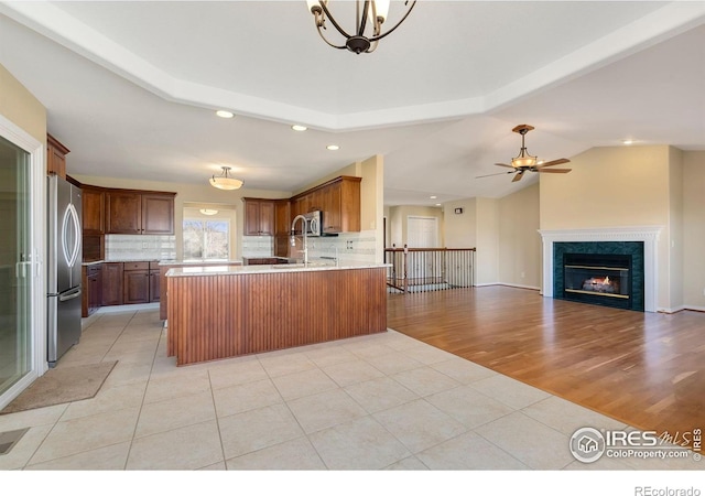 kitchen with appliances with stainless steel finishes, a high end fireplace, light tile patterned flooring, decorative backsplash, and vaulted ceiling