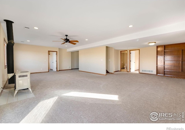 carpeted empty room featuring a wood stove and ceiling fan