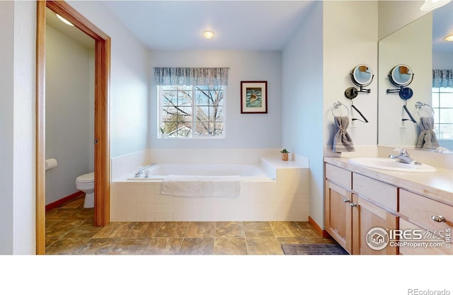 bathroom with a relaxing tiled tub, vanity, and toilet