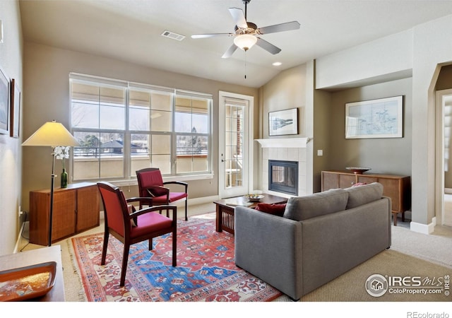 carpeted living room with ceiling fan, a tile fireplace, and vaulted ceiling