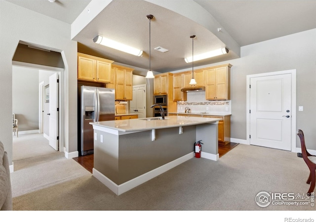 kitchen featuring an island with sink, decorative light fixtures, sink, appliances with stainless steel finishes, and light brown cabinetry